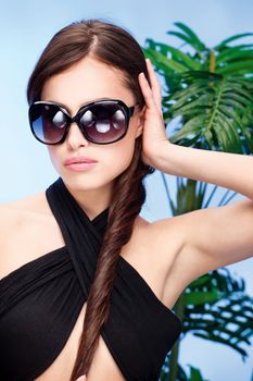 Pretty woman with big sun glasses and long hair in front of a palm tree