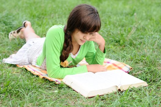 Girl reading a book lying on the grass