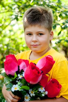 A boy with a bouquet of artificial flowers in summer park