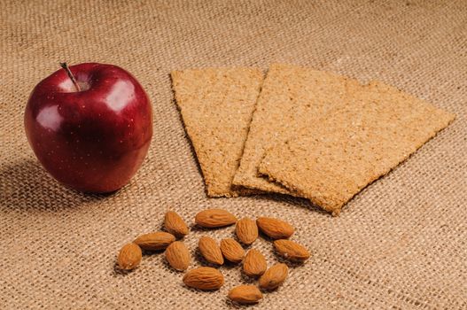 Red apple with crispbread and almonds on sacking background