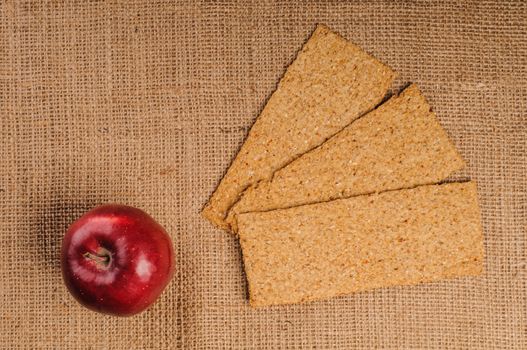 Red apple with crispbread on sacking background