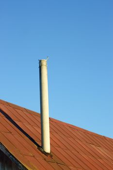 Chimney on an old tinny roof against the blue sky