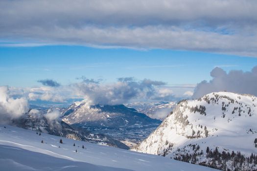 Snow-covered mountains in the French Alps with a slope in the foreground, sunlight and also some grey clouds in the background.