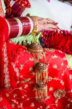 Bride is sitting in red wedding dress and lots of bracelets in her arms and flowers in her lap