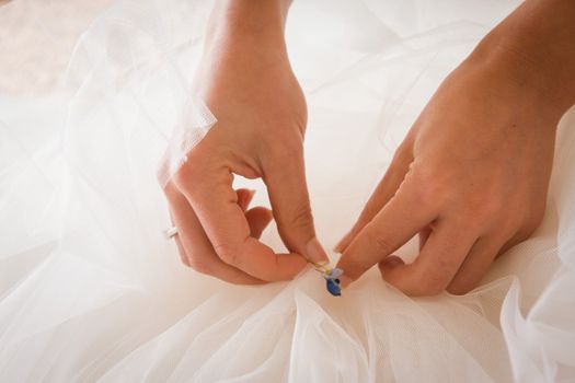 Close-up on a bride's hands as she is putting a little blue textile on her white wedding dress according to the english "something old-new-borrowed-blue" custom.