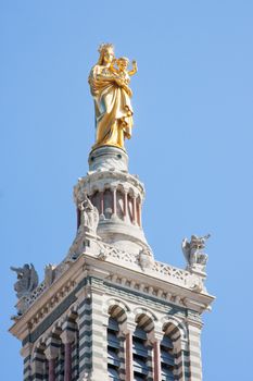 A golden statue of the Madonna holding the little Jesus on the top of a tower of the basilica, Notre-Dame de la Garde in Marseilles, in a sunny day with clear blue sky in the background