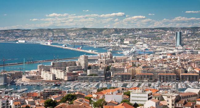 A landscape of Marseille from above with the see and mountains and white clouds in the background