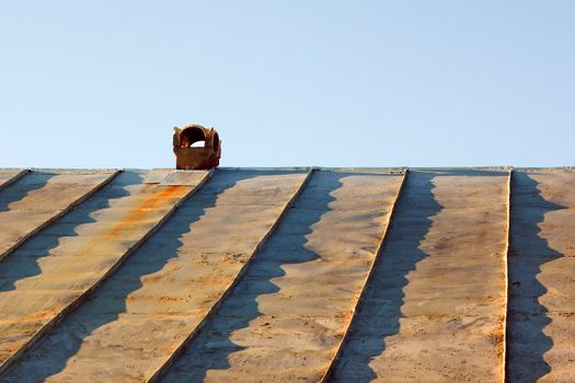 Chimney on an obsolete tinny roof against the blue sky