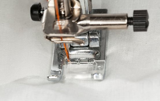 Sewing machine macro sews cloth with orange cotton thread