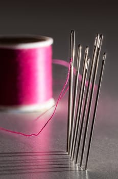 Row of sewing embroidery needles with red thread and shadows with bobbin