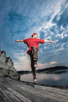 A male young dancer jumping and forming a cross in the evening by the sea