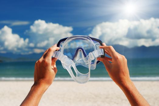 Snorkel equipment in hands against beach and sky