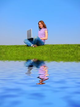 Girl with notebook sitting on grass against sky with reflection on water