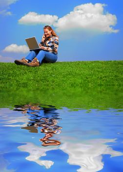 Girl with notebook sitting on grass against sky with reflection on water