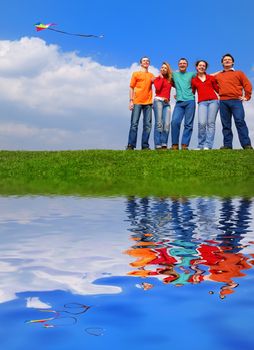 Group of people smiling against blue sky with reflection on water