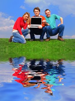 Group of people with notebook sitting on grass against sky with reflection on water