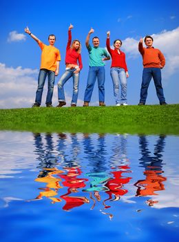 Group of people with thumbs up against blue sky with reflection on water