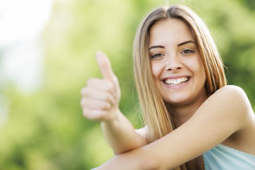Young smiling blond female outdoors showing thumb up sign