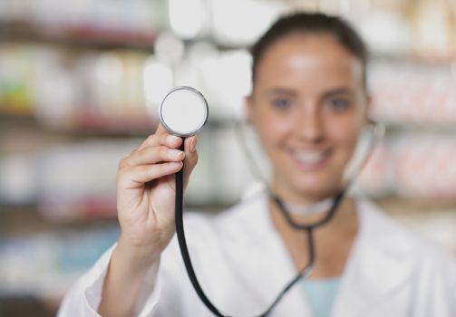 Young woman doctor holding stethoscope in pharmacy, shallow depth of field