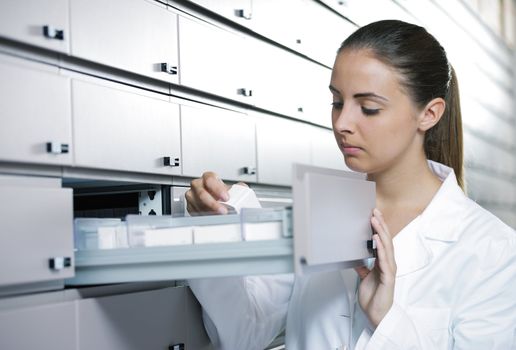 Young woman pharmacist taking medicine from drawer