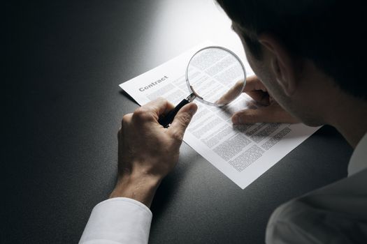 Young businessman looking to a contract through a magnifying glass 