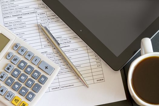 Modern workplace with digital tablet showing charts and diagram on screen, coffee, pen and paper with numbers.