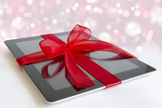 Digital tablet with red ribbon gift isolated on white.