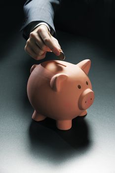 Businessman hand putting coin into a piggy bank