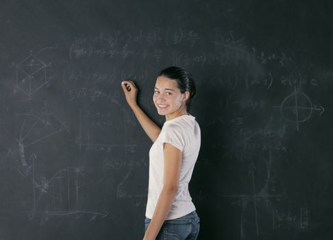 A young female student is standing in front of the blackboard going to draw something with a chalk.