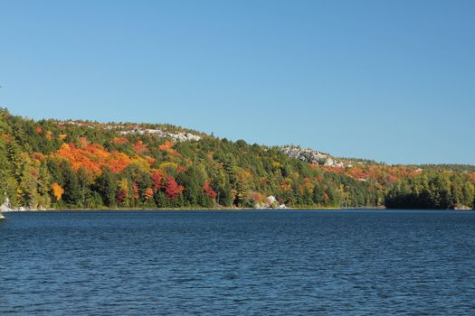 Autumn landscape. Rocky ridges, colourful trees and clear blue lake
