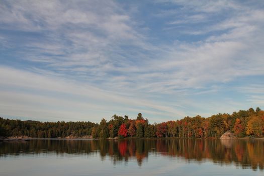 Bright coloured foliage trees reflecting on calm lake, Ontario, Canada – HDR shot
