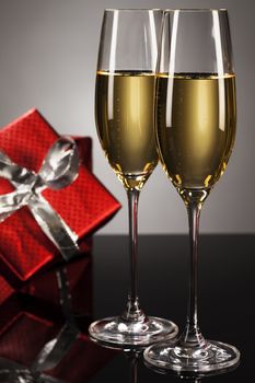 two glasses of champagne with a red present in background on a mirror
