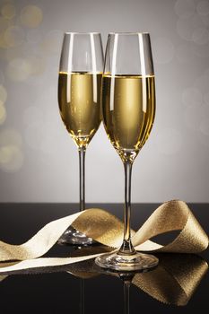 two glasses of champagne with a golden ribbon on a mirror with a spot light background