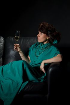 Beautiful girl sitting on a sofa with glass of wine, black background