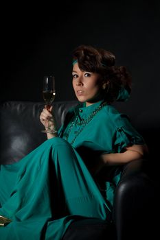 Beautiful girl sitting on a sofa with glass of wine, black background