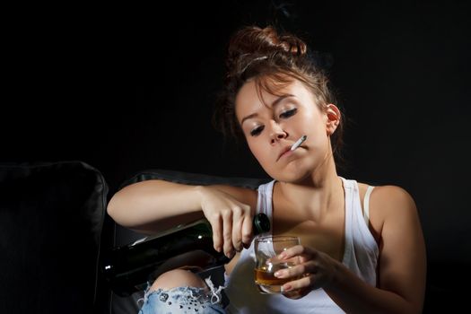 Closeup dark portrait of a woman smoking with a cigarette hanging out of her mouth while pouring a herself an alcoholic drink