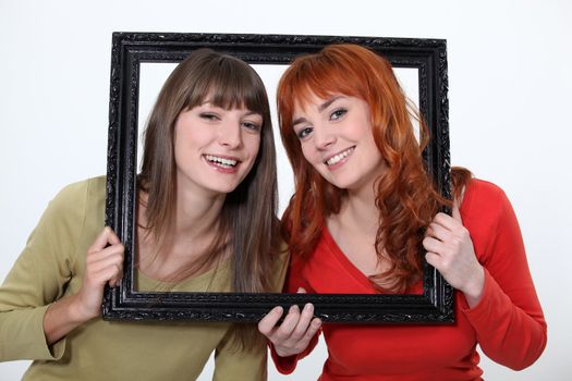 Women poking heads through empty picture frame