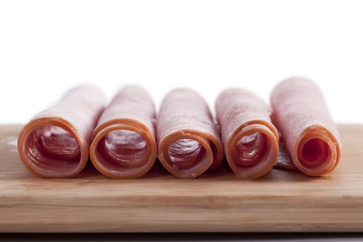 Horizontal image of ham rolls on a chopping board against white background
