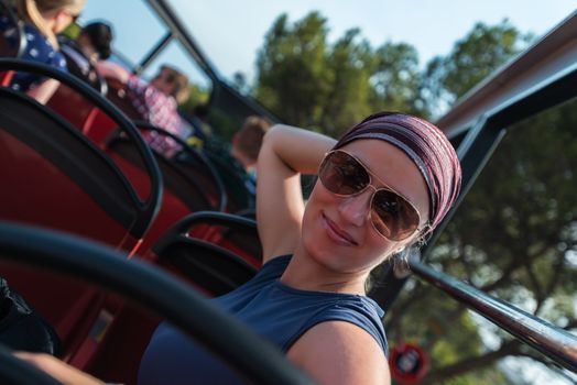 Smiling woman on tourist bus in sunglasses and bandana. Shallow depth of field.