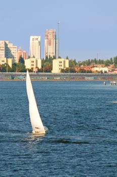 Vessel ship with white sails on water with urban scene as background