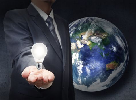 businessman holds light bulb to glowing the earth