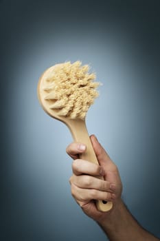 Man holding a brush made of wood and natural fibers in his hand.