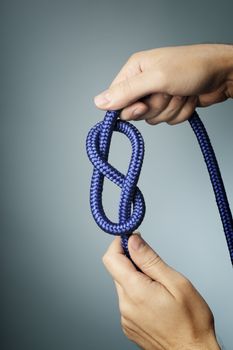 Man holding blue rope with figure of eight knot in his hands.