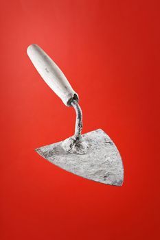 Old dirty trowel tool on red background.