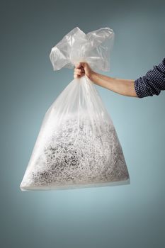 Man holding a transparent plastic bag with shredded paper.