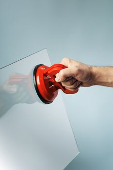 Man lifting a sheet of glass using a vacuum suction cup tool aka dent puller.