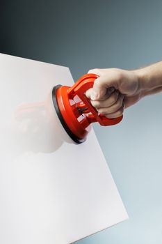 Man lifting a white ceramic tile using a vacuum suction cup tool aka dent puller.