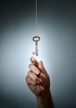 Conceptual image of a hand taking an old key hanging from a string.
