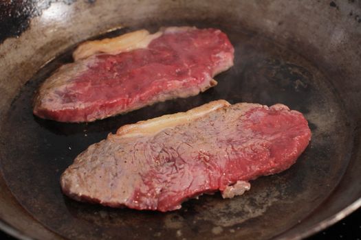 Beef steak cooking in a iron grill pan.