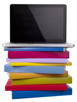 A laptop on top of a stack of colourful books.